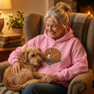 Older woman in cozy pink bear graphic hoodie sitting with dog by fireplace