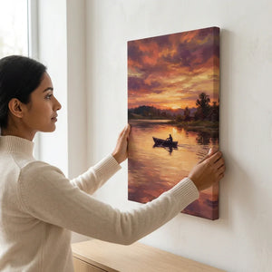 Woman hanging canvas wall art of a sunset lake scene with a boat and trees.