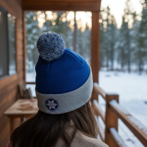 Woman in blue pom pom beanie with snowflake patch on snowy cabin porch