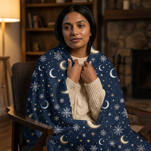 Woman in cozy living room wearing navy throw blanket with moon and snowflake pattern