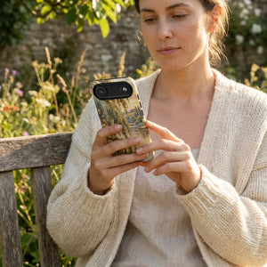 Woman in cozy cream sweater using smartphone with nature-inspired case outdoors