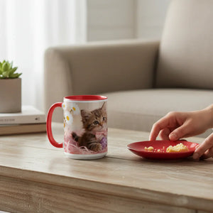 Ceramic mug with kitten design and red handle on coffee table beside red plate with crumbs
