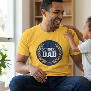 Smiling man wearing yellow Number 1 Dad t-shirt playing with young child indoors
