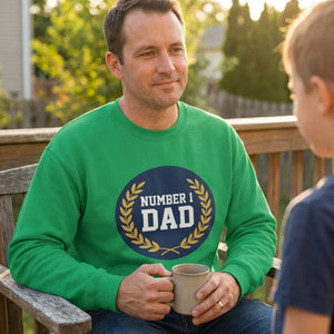 Man in green Number 1 Dad sweatshirt holding mug outdoors with child