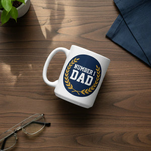 White ceramic mug with 'Number 1 Dad' design on wood desk, near glasses and plant
