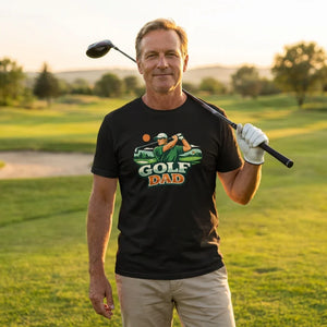 Man on golf course wearing black 'Golf Dad' graphic t-shirt, holding golf club and smiling