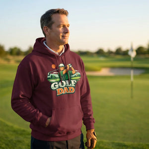 Man wearing maroon Golf Dad hoodie standing on golf course at sunset