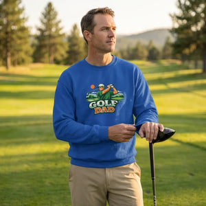 Man on golf course wearing blue 'Golf Dad' sweatshirt, holding golf club