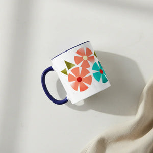 White ceramic mug with colorful geometric flower pattern and blue handle on light surface