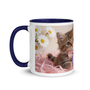 White ceramic mug with dark blue handle and rim, featuring a kitten with a pink bow and daisies.