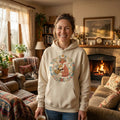 Smiling woman in a cozy living room wears a cream hoodie with a fox and floral design.