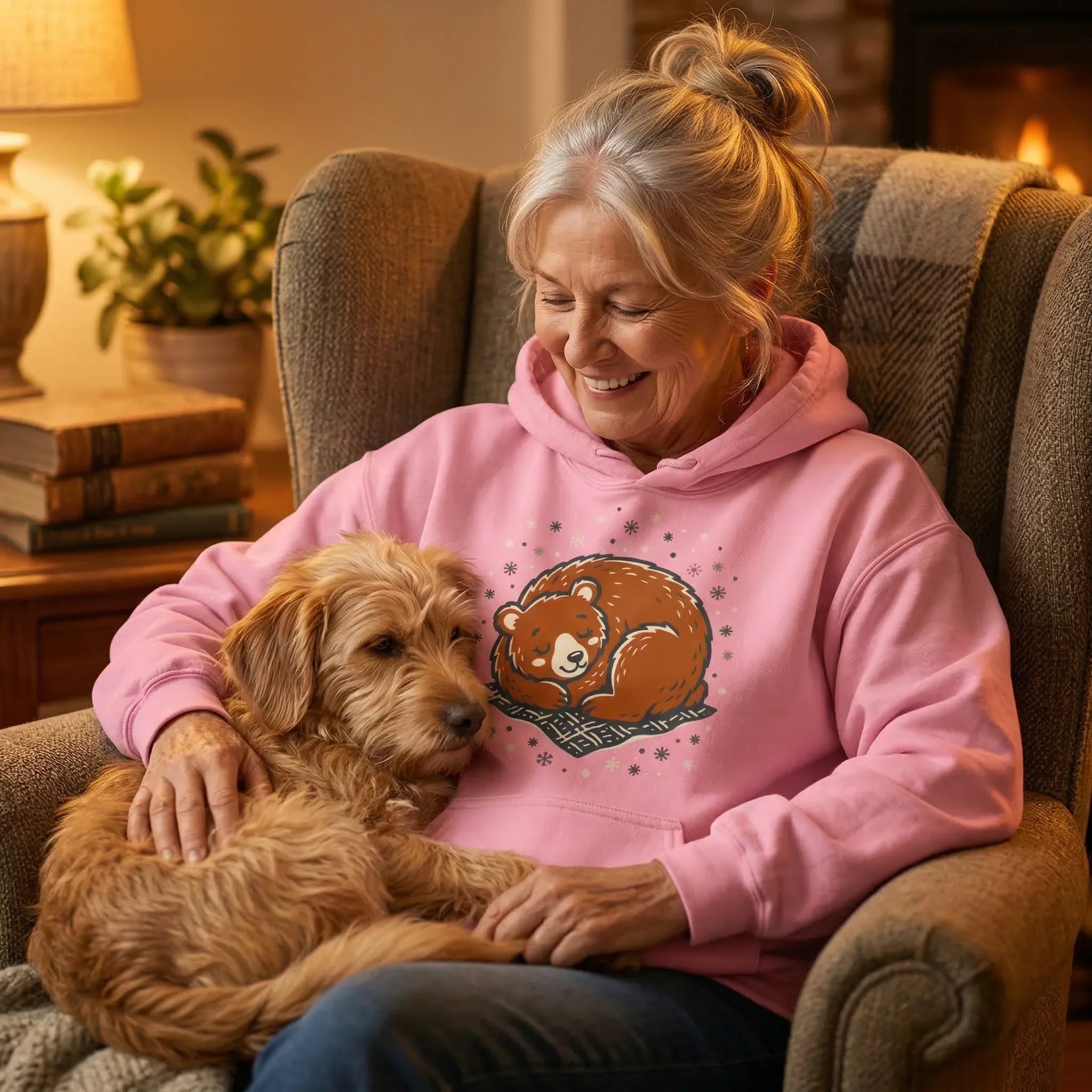 Older woman in cozy pink bear graphic hoodie sitting with dog by fireplace