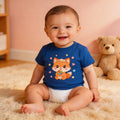 Smiling baby in blue fox graphic t-shirt and diaper sitting on plush rug with teddy bear
