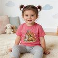 Smiling toddler girl in a pink animal graphic t-shirt and leggings in a cozy room.
