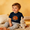 Smiling young boy in navy bear graphic t-shirt and sweatpants sitting with plush bunny.