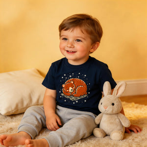 Smiling young boy in navy bear graphic t-shirt and sweatpants sitting with plush bunny.