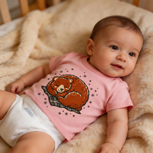 Baby wearing pink bear graphic t-shirt and diaper on soft beige blanket
