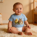 Baby in blue animal graphic t-shirt and diaper sitting on soft rug in cozy nursery
