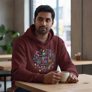 Man in a maroon hoodie with colorful gamer-themed birthday graphic, sitting at a cafe table with coffee.
