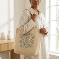 Woman holding a canvas tote bag with colorful floral and vegetable design in a bright room