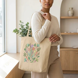 Woman holding a beige tote bag with colorful floral and vegetable illustration, home goods decor