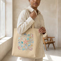 Woman holding beige tote bag with colorful seashell and starfish illustration in a bright room