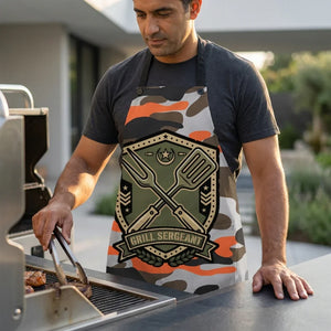 Man grilling outdoors wearing a camo 'Grill Sergeant' BBQ apron, holding tongs by grill.