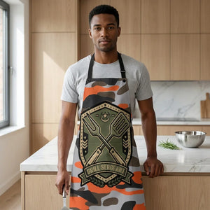 Man in kitchen wearing camo apron with 'Grill Sergeant' badge, holding barbecue spatula