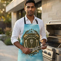 Man in outdoor kitchen wearing novelty grilling apron, holding tongs by gas grill