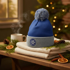 Blue and gray pom pom beanie with snowflake patch, cozy holiday decor, pine and cup of coffee