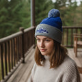 Woman in cozy knit sweater and blue mountain pom beanie on wooden porch outdoors