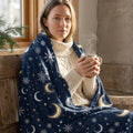 Woman cozy in knit sweater and celestial moon blanket, holding steaming mug indoors