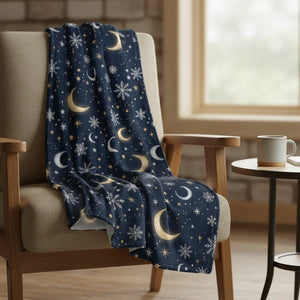 Cozy navy throw blanket with gold moons and white snowflakes draped over a beige armchair