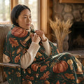 Woman wrapped in cozy fall-themed blanket with pumpkins and candles in rustic living room