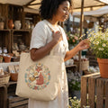 Woman holding floral fox canvas tote bag at outdoor market, picking daisies