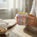 Person holding a cute bunny mug with an Easter egg design on a sunlit wooden table.