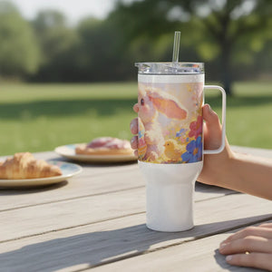 Easter-themed travel mug with bunny and chick design, outdoor picnic setting, pastries nearby